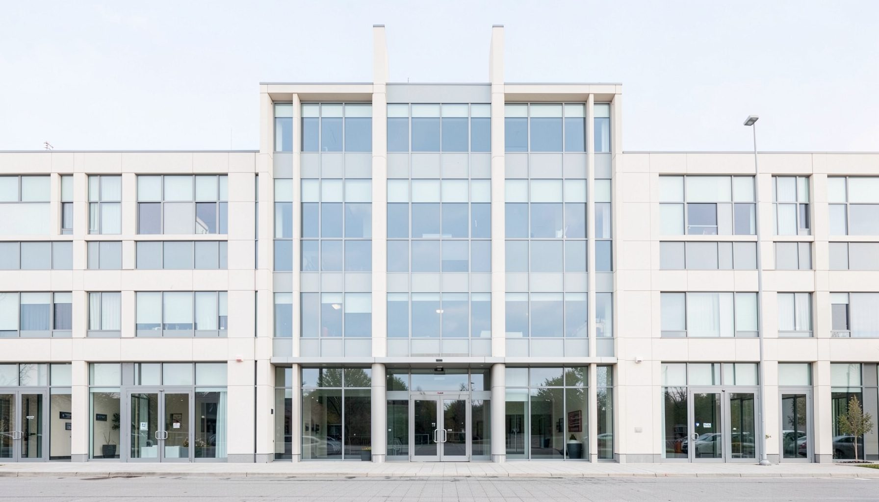 A clean, symmetrical architectural photograph of a modern hospital building facade with large glass windows and a calm, neutral color palette of whites, soft grays, and pale blues, conveying a sense of order and professionalism.