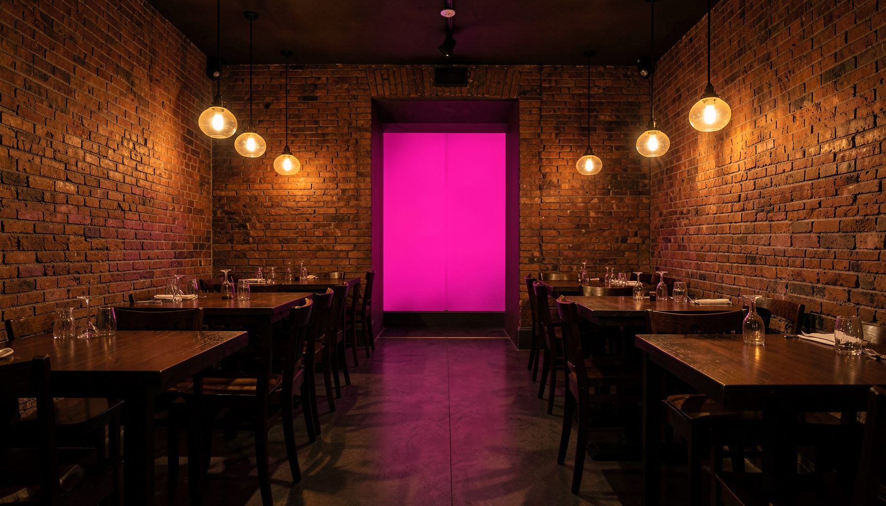 Warmly lit restaurant interior with dark wood tables, exposed brick walls, and soft amber pendant lighting creating an intimate dining atmosphere.